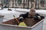 An elderly woman searches a dumpster for food.