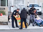 Police carry a protester away from the ICE facility. To the right, police arrest a protester after covering the person's face and ears.