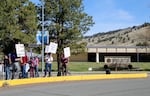 A cluster of people holding picket signs stand on a sidewalk near a building with a sign out front that reads "Oregon Institute of Technology."