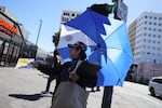 A woman covers herself from the sun while handing out fliers during an unseasonably hot day at MacArthur Park on Thursday, March 12, 2026, in Los Angeles. The heat dome impacting California and other states is heading to Oregon.