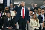 President rump stands and salutes, flanked by Secretary of Defense Pete Hegseth and First Lady Melania Trump.