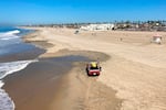 A vehicle drives along a sunny expanse of sandy beach.