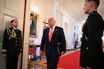 In this photo, President Trump is walking into the White House's East Room. Behind him is a wide hallway with a long red carpet.