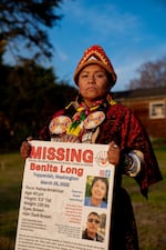 In this photo, Loni Long is outdoors and holding a missing-person sign with details about her missing cousin, Benita Long. Loni Long is wearing traditional Indigenous clothing.