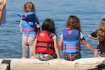 Three young girls rest on a log at Owen Beach on July 30, 2024. They watch as canoes land on their second to last day of the 2024 Canoe Journey.