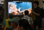 People at a train station in Seoul watch a TV screen.