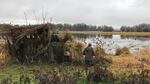 Two men wearing camo stand behind a shelter hunting ducks.