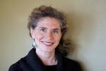 middle aged woman, curly hair tied back, smiling at camera