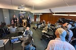 In this photo taken with a smartphone, Mike Herrington, the FBI special agent in charge, speaks to the media on Tuesday, Oct. 6, 2026, in Seattle. Standing next to Herrington are Elija Rain, the assistant commissioner of the British Columbia Royal Canadian Mounted Police, left, and Acting U.S. Attorney Neil Floyd, right.