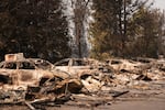 A line of burned cars sit in a parking lot Tuesday, Aug. 4, 2026, after a wildfire hit the northern part of Spokane, Wash.