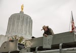 A man holding a sign in opposition to Oregon House Bill 2020 talks to fellow rallygoers from the roof of a truck at an event on the Oregon Capitol steps in Salem, Ore., on Thursday, June 27, 2019.