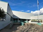 The outside of Creston K-5 school in Southeast Portland. There is a ramp and stairs to the front doors. A flag waves on a pole to the right. The sky is blue with clouds in the corner.