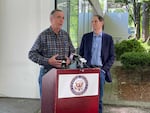 US Senators Ron Wyden and Jeff Merkley wear informal clothes as they speak at a podium.