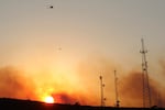 A helicopter carries water on a longline to a wildfire near Salem, Ore., at sunset Friday, Sept. 9, 2022. By Saturday morning, skies across much of Western Oregon were tinged with a pinkish-yellow haze due to a heavy blanket of smoke.