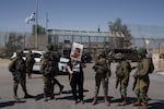 A woman holds up a sign for a hostage held captive by Hamas in Gaza as she stands next to Israeli soldiers at Israel's Nitzana border crossing with Egypt in southern Israel on Tuesday, March 5, where the group protests the delivery of humanitarian aid to Gaza until all of the hostages being held by Hamas militants have been released.