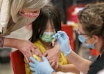 Kelly Leung, 11, center, is reassured by Multnomah County Deputy Health Officer Dr. Ann Loeffler, left, and Sarah Roy, RN, as Leung receives vaccinations at McDaniel High School in Northeast Portland on Feb. 8, 2023. 