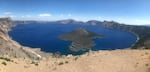 A panorama view of Crater Lake on a sunny day with Wizard Island in the center.