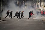 Demonstrators run across a street during an anti-government protest in La Paz, Bolivia, Monday, May 18, 2026.