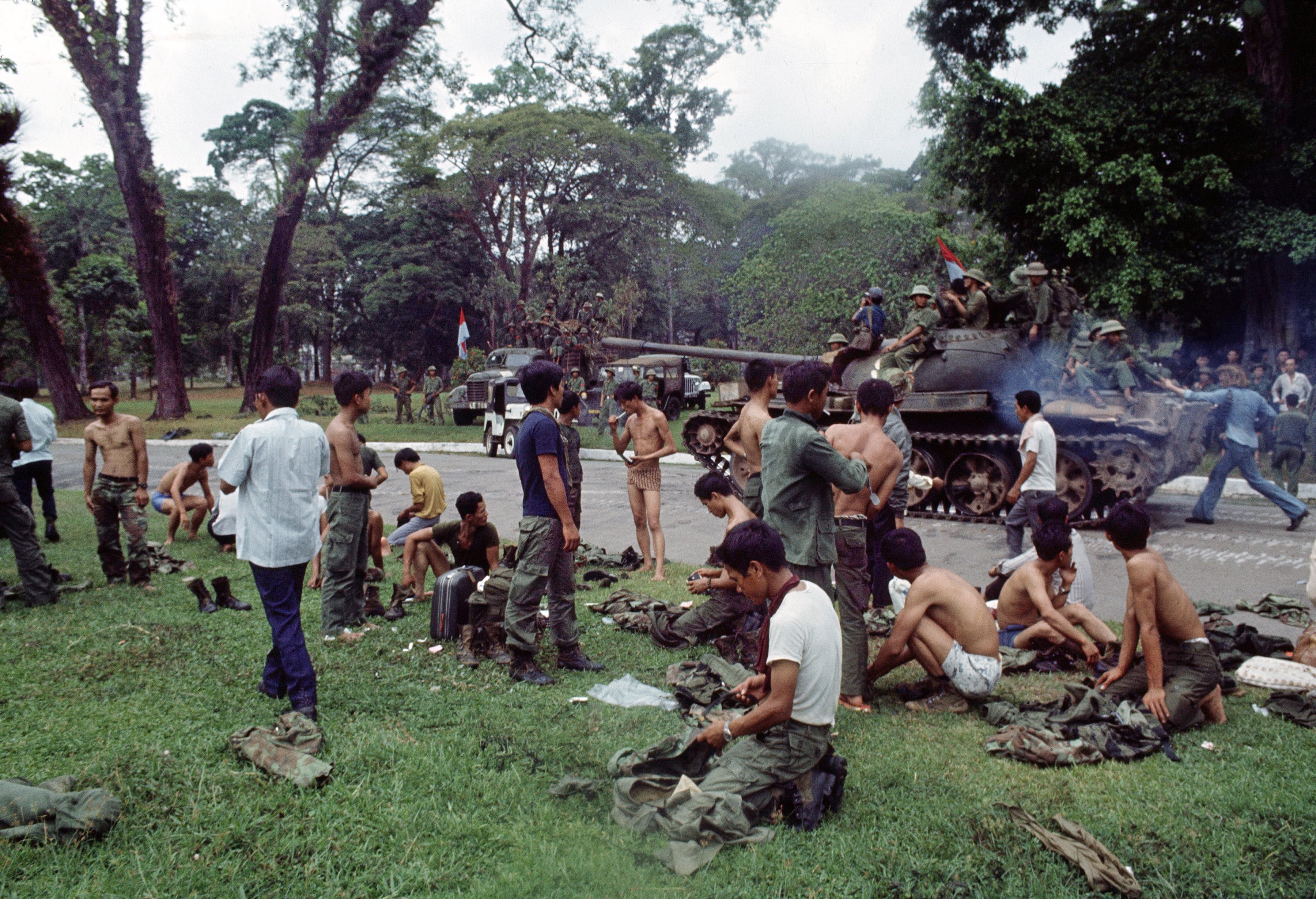 As victorious North Vietnamese troops ride past on a tank, defeated South Vietnamese troops discard their uniforms in Saigon on April 30, 1975, the day the South Vietnamese capital fell to communist forces, ending the Vietnam War.