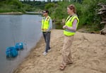 A man and woman stand next to a river wearing yellow safety vests.