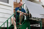 Sitting outdoors on his back steps, which are metal and painted green, Craig Keenan installs a plug-in solar panel in front of the railing at the top.