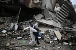 A Palestinian carries some of his belongings on Thursday, March 7, as he walks by buildings destroyed in Israeli bombing after returning briefly to Khan Younis, in southern Gaza, to check on what remains of his home.