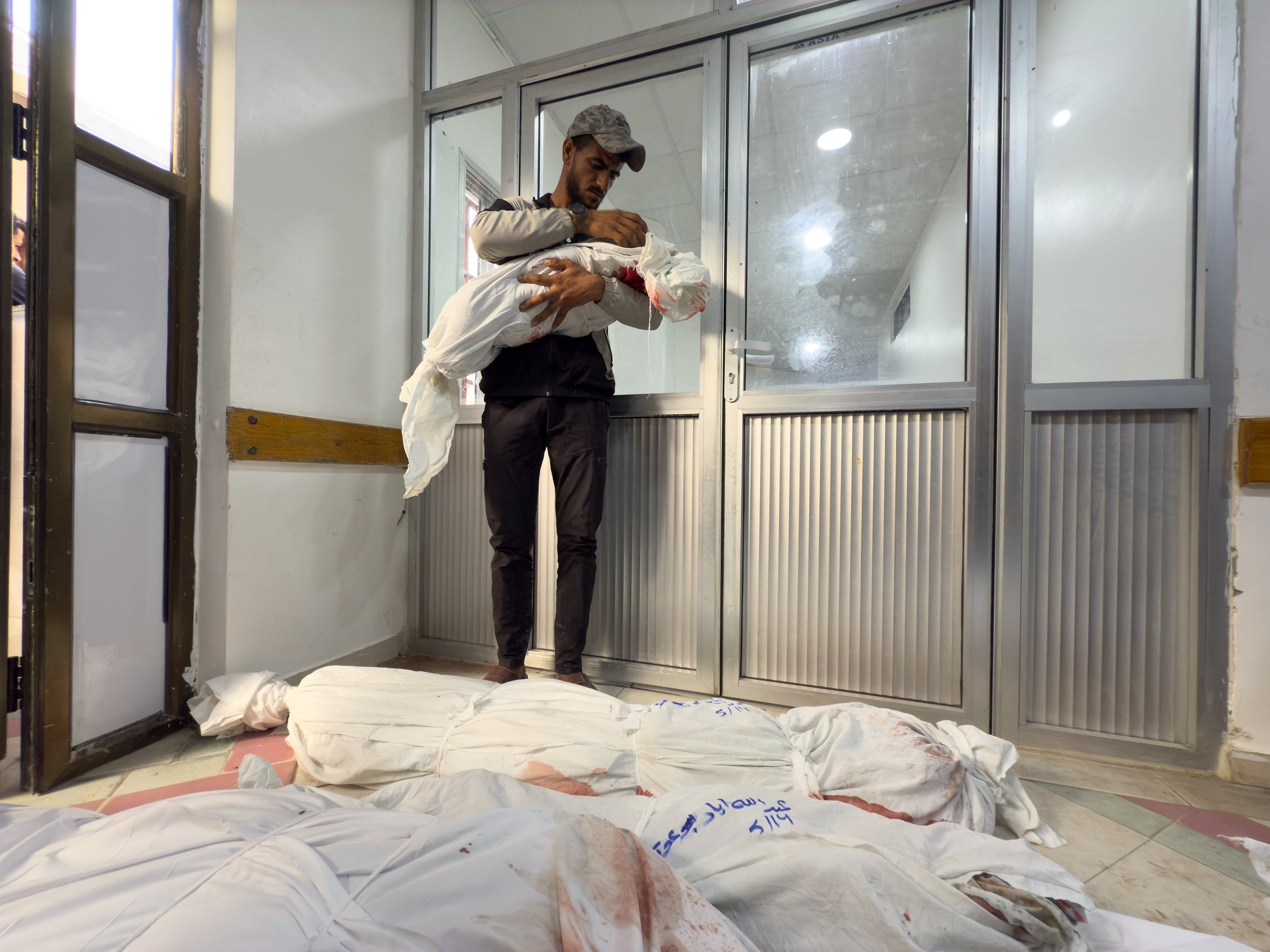 A man holds a small child's corpse wrapped in shroud, with other wrapped bodies lying on the floor, in the Indonesian Hospital in Jabalia, in northern Gaza Strip, Wednesday.