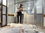 A man holds a small child's corpse wrapped in shroud, with other wrapped bodies lying on the floor, in the Indonesian Hospital in Jabalia, in northern Gaza Strip, Wednesday.