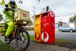 A postman rides a bicycle past Australia Post red and yellow Australia Post mailboxes Melbourne, Australia.
