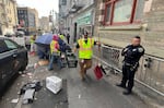 San Francisco police officers keep an eye on city workers as they sweep unsanctioned tents and belongings from a street in the Tenderloin