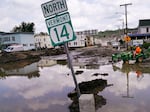 A small tractor clears water from a business as flood waters block a street, July 12, 2023, in Barre, Vt. Vermont has become the first state to enact a law requiring fossil fuel companies to pay a share of the damage caused by climate change after the state suffered catastrophic summer flooding and damage from other extreme weather.