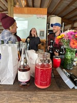 A jug of fresh Airlie Red Flesh apple juice sits next to an Alpenfire Cider made from the same apple variety, while cider makers Christine Walter (L) and Levi Danielson (R) sample ciders on the RainShine Family Farm. October 21, 2024.  