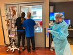 Two visitors peer into the room of a COVID-19 patient in the intensive care unit at Salem Hospital in Salem, Oregon, on Friday, Aug. 20, 2021, as a nurse dons full protective gear before going into the room of another patient. The hospitalization rate of unvaccinated COVID-19 is breaking records and squeezing hospital capacity, with several running out of room to take more patients.