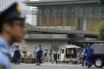 Police officers work near a vehicle, center, which was stuck against a barricade near the prime minister's office, background, in Tokyo on Saturday.