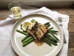Cooked white fish on a bed of asparagus, with a glass of white wine.