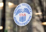  This photo shows the Social Security Administration logo on a glass window of a Social Security Administration office in Washington, D.C., in March. The round white logo features a blue eagle, the letters "USA" in red in the middle and the words "SOCIAL SECURITY ADMINISTRATION" in blue around the border of the circle.