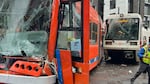 An orange street car with a destroyed windshield and a light rail train with a cracked windshield.