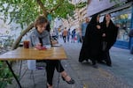 A woman sits in the al fresco dining area of a cafe at the Enqelab-e-Eslami (Islamic Revolution) street, in Tehran, Iran, Saturday, Sept. 27, 2025.