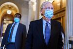 Mitch McConnel, wearing a face mask, his eyeglasses and a dark suit, walks through the U.S. Capitol, while another man, also wearing a facemask and suit, walks just behind him.