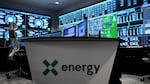 A desk with the X-energy logo is surrounded by computer displaying various graphs and data.