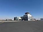 A small plane refuels in front of a modestly sized airport in front of a clear blue sky.