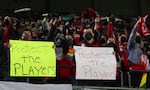A pair of Portland Thorns fans hold signs that say "Protect the players" during the first half of the team's NWSL soccer match against the Houston Dash in Portland, Ore., Wednesday, Oct. 6, 2021.