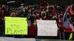 A pair of Portland Thorns fans hold signs that say "Protect the players" during the first half of the team's NWSL soccer match against the Houston Dash in Portland, Ore., Wednesday, Oct. 6, 2021.