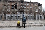 A local resident looks at a damaged apartment building during heavy fighting near the Illich Iron & Steel Works Metallurgical Plant, the second largest metallurgical enterprise in Ukraine, in an area controlled by Russian-backed separatist forces in Mariupol, Ukraine, Saturday, April 16, 2022. Mariupol, a strategic port on the Sea of Azov, has been besieged by Russian troops and forces from self-proclaimed separatist areas in eastern Ukraine for more than six weeks.