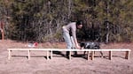 A woman leads a dog along a low wooden table with empty jars, one of which contains wolf scat.