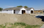 Three houses in various states of construction line a neighborhood road, with a large pile of dirt in the foreground.
