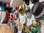 A shot from the side of a white wall with pegs. A variety of multi-colored hats, masks and headpieces hang on hooks.