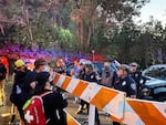 Protesters in face coverings and baseball caps stand on one side of a traffic barrier, facing   uniformed police officers and several people not in uniforms on the other side of the barrier.