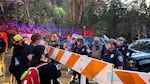 Protesters in face coverings and baseball caps stand on one side of a traffic barrier, facing   uniformed police officers and several people not in uniforms on the other side of the barrier.