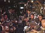 A group of Black men in military uniforms face the camera from the inside of an airplane.